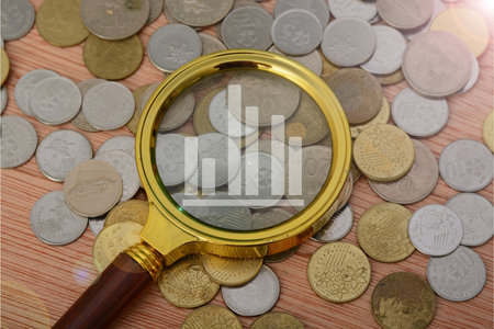 The financial analyst examined the money market trends through a magnifying glass, carefully scrutinizing the coin-shaped data points on the graphの写真素材