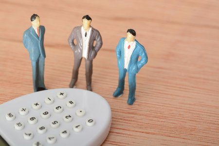 The businessman, standing in a row with colleagues, used a calculator as he thought about the cost implications in the industryの写真素材