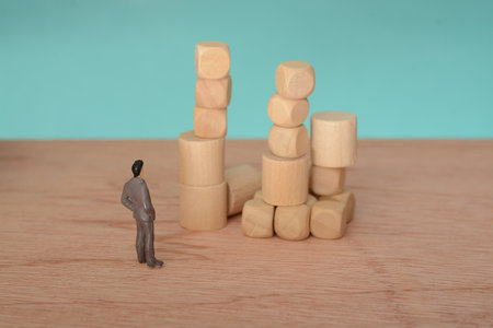 The businessman, deep in thought and surrounded by wooden blocks, pondered the problem and the challenge of development, searching for a solution for the companyの写真素材