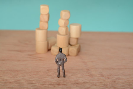 The businessman, deep in thought and surrounded by wooden blocks, pondered the problem and the challenge of development, searching for a solution for the companyの写真素材