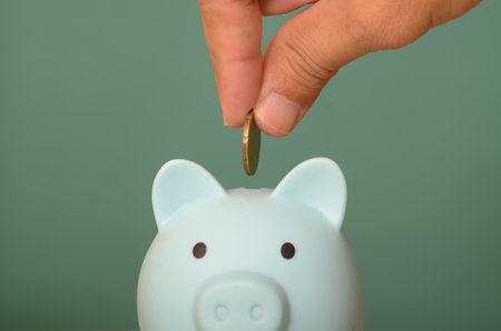 The image of a hand holding money to place in a piggy bank symbolizes the act of saving and financial responsibility.の写真素材