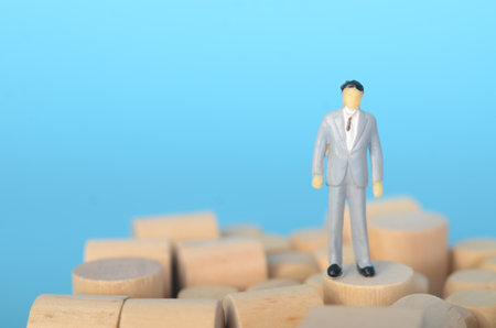 A businessman precariously balanced on a wooden block symbolizes the challenges and uncertainties...