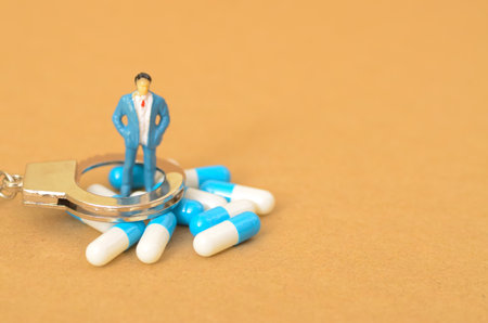 the potential legal consequences of drug trafficking and possession, symbolized by the miniature businessman standing on handcuffs amidst a pile of pills.の写真素材