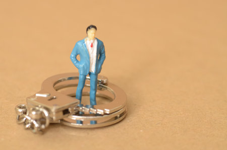 The miniature businessman standing on the handcuffs near the money symbolizes the potential consequences of engaging in bribery, including legal repercussions.の写真素材