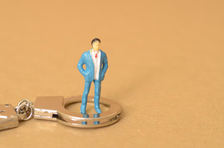 The miniature businessman standing on the handcuffs near the money symbolizes the potential consequences of engaging in bribery, including legal repercussions.の写真素材