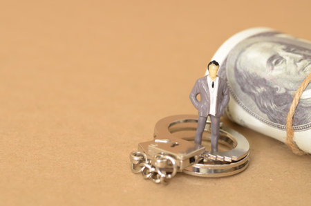 The miniature businessman standing on the handcuffs near the money symbolizes the potential consequences of engaging in bribery, including legal repercussions.の写真素材