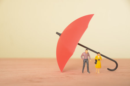A man and woman, both sheltered under umbrellas, symbolize the protection provided by insurance...