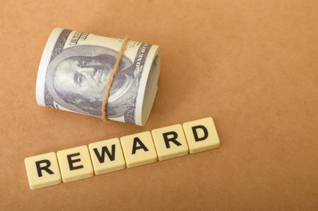 The image visually represents the concept of a reward, with the word "REWARD" spelled out in tiles and accompanied by a roll of money.の写真素材
