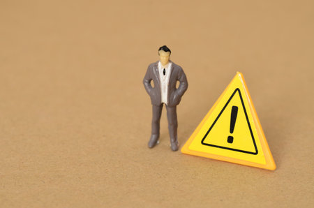 A stern-faced businessman, standing tall and resolute, gazes into the distance, with a warning exclamation mark nearby, signaling impending danger.の写真素材