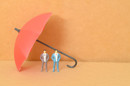 The two businessmen, standing side by side beneath a large red umbrella, symbolize the partnership and protection they provide each other in their endeavors.の写真素材