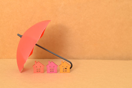 The red umbrella, sheltering three miniature houses, symbolizes the protection and security that home insurance provides.の写真素材