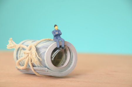 The businessman, seated atop a pile of money banknotes, is deep in thought, strategizing his next target for financial gain.の写真素材