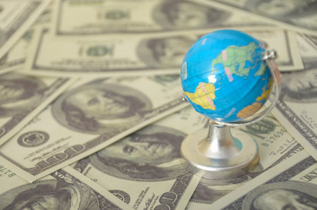 The globe, a symbol of international relations, is dwarfed by the abundance of money, highlighting the importance of economic power.の写真素材