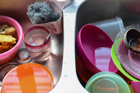 The image shows a stainless steel kitchen sink filled with dirty dishes and utensils.の写真素材