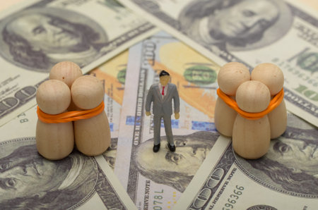 wooden figures bound together on a bed of dollar bills symbolizes the exploitation and commodification of human beings in the context of human trafficking.の写真素材