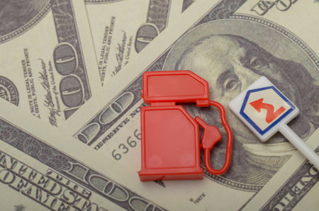 A toy gas pump and a sign symbolizing rising fuel prices rest atop a bed of US dollar bills, highlighting the increasing cost of gasoline.の写真素材