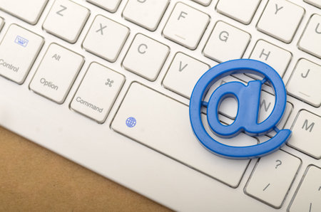 A blue plastic "@" symbol rests on a white computer keyboard, highlighting the importance of email in modern communication.の写真素材
