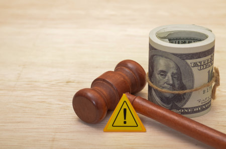 A gavel lies next to a roll of dollar bills, with a warning sign bearing an exclamation mark, suggesting potential financial legal issues.の写真素材