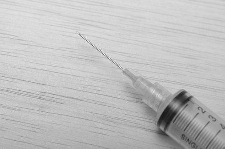 Black and White Close-Up of a Medical Syringe with Needle on Textured Surfaceの写真素材