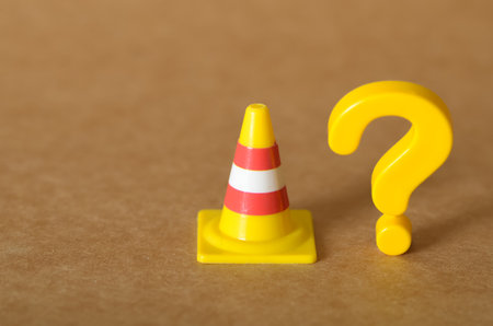 Questioning Roadblocks: Yellow Toy Traffic Cone and Question Mark on Neutral Backgroundの写真素材