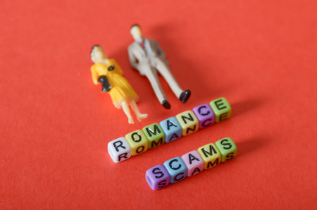 Romance Scams Concept with Miniature Couple and Letter Blocks on Red Backgroundの写真素材