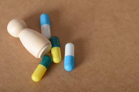 Medical Concept: Wooden Figure and Assorted Capsules Depicting Medication Effects and Health Implicationsの写真素材