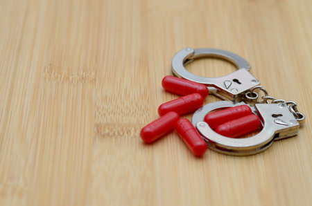Red Pills Inside Handcuffs Represent Drug Arrest and Legal Consequencesの写真素材