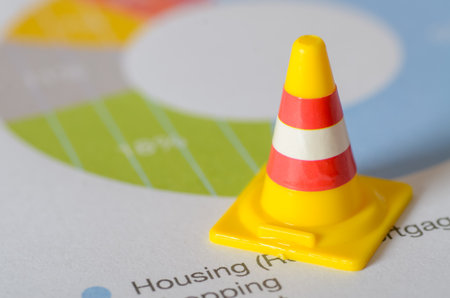 Financial Caution: Miniature Traffic Cone on a Budget Pie Chart Symbolizing Risk in Housing and...