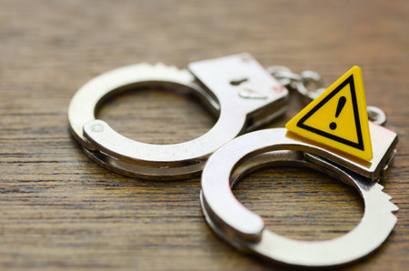 A Stark Warning: Shiny Handcuffs and a Bright Yellow Sign Symbolizing the Severe Legal Consequences of Crime.の写真素材