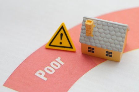a house next to a yellow warning sign on a document with a Poor rating, symbolizing the dangers of...
