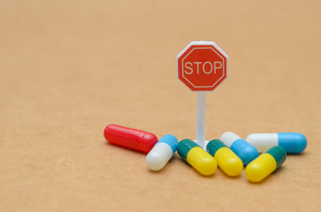 A red "STOP" sign surrounded by colorful medicinal capsules creates a powerful visual metaphor for the dangers of addiction and pharmaceutical overuse.の写真素材