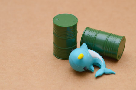 A blue narwhal figurine lies before two green barrels, a stark visual metaphor for the devastating impact of chemical waste on vulnerable ocean species.の写真素材