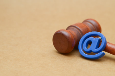 A blue @ symbol leans against a judge's gavel, powerfully symbolizing the intersection of cyber law,...