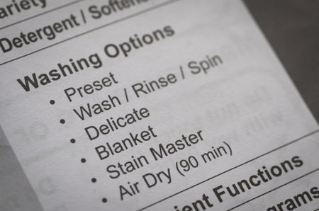 The "Washing Options" section of an appliance manual is in sharp focus, clearly displaying cycles like "Delicate," "Blanket," and "Air Dry" for proper use.の写真素材