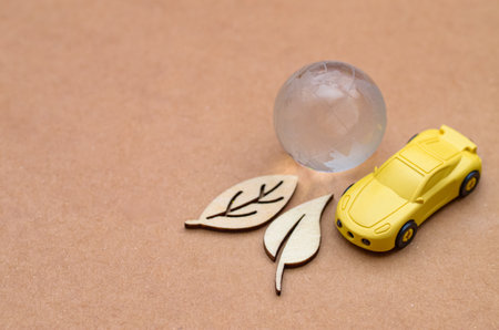 A clear glass Earth globe, a car, and wooden leaves symbolize the vital connection between eco-friendly transportation and global environmental health.の写真素材