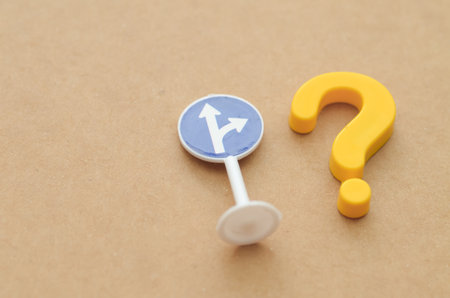 A road sign showing a split path is paired with a yellow question mark, symbolizing the confusion and critical choices faced when life's direction is unclear.の写真素材