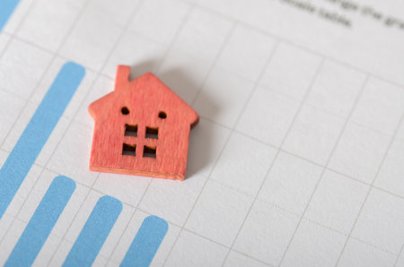 A small house figurine on a bar graph, visually representing the rising value of property and residential assets.の写真素材