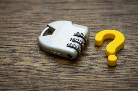 A combination padlock sits beside a bright yellow question mark, symbolizing a complex problem or secret that requires the right answer to be unlocked.の写真素材