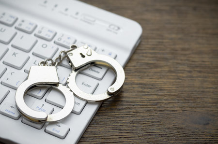 Handcuffs on a keyboard symbolize the real-world legal ramifications of illegal online activities like hacking and fraud.の写真素材