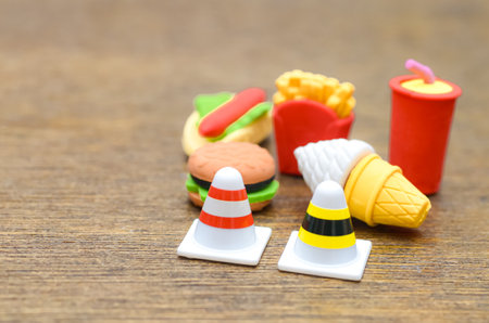 Stop Unhealthy Eating: A conceptual image using traffic cones to block a miniature hamburger, fries, and soda, representing the need for diet and nutritional awareness.の写真素材