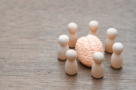 The Power of the Mastermind: A team of peg figures surrounds a central brain model, representing a collective focus or a brainstorming session.の写真素材