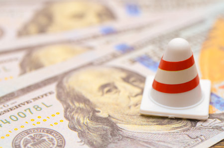 Caution: Money Matters: A traffic cone placed on hundred-dollar bills serves as a stark warning for financial planning and economic risks.の写真素材