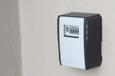 A key lockbox with a code is fixed to a pale wall, symbolizing controlled access and home security.
