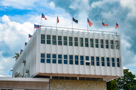Malaysian Pride: Numerous Malaysian flags fly from a formal white building under a dramatic, cloudy...