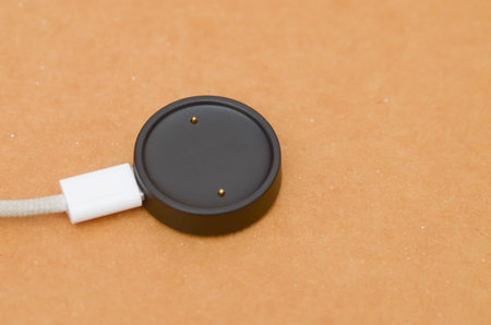 black magnetic charging puck, commonly used for smartwatches. A white cable with a braided texture extends from the left side of the chargerの写真素材