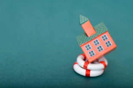 Home Insurance Concept: Miniature Toy House with Pink Roof Protected Inside Red and White Lifebuoy Ringの写真素材