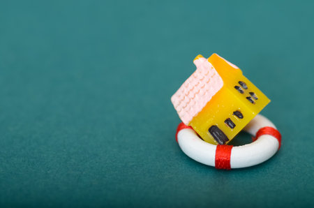 Concept of Home Insurance and Property Safety: Toy House Secured by a Lifebuoy on Teal Backgroundの写真素材