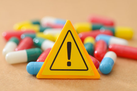 Yellow Triangular Warning Sign with Exclamation Mark Standing in Front of Colorful Pharmaceutical Capsules Pileの写真素材
