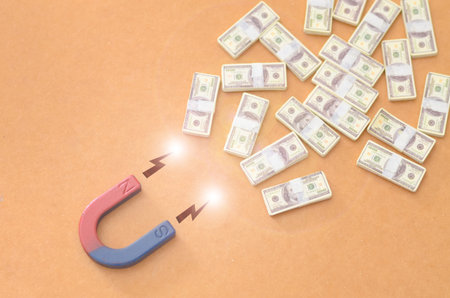 Conceptual Visualization of Wealth Attraction: A Magnet Drawing Miniature Money Stacks with Glowing Lightning Bolts on Ochre Background.の写真素材