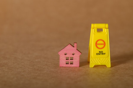Restricted Property Access Metaphor: Small Yellow No Entry Warning Sign Beside a Simple Wooden Home Symbolの写真素材